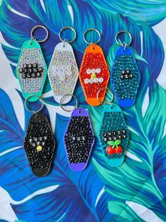 six keychains with different designs on them sitting in front of a palm leaf