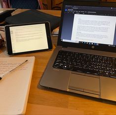 an open laptop computer sitting on top of a wooden desk next to a note pad