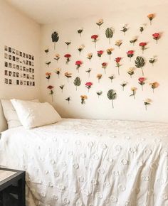 a white bed sitting in a bedroom next to a wall mounted with flowers on it