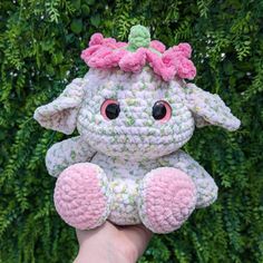 a crocheted stuffed animal with a pink bow on it's head sitting in front of some bushes