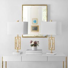 a white console with gold trim and two lamps on each side, in front of a mirror