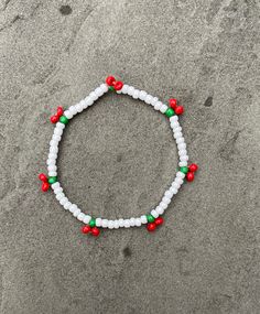 a white beaded bracelet with red and green beads sits on the sand at the beach