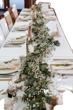 a long table is set with place settings and greenery