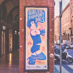 an old poster advertises girls support girls on the side of a brick building