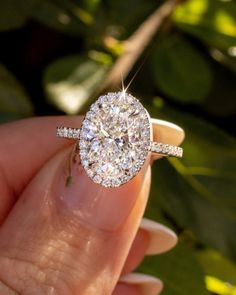 a woman's hand holding a diamond ring in front of her face with leaves behind it