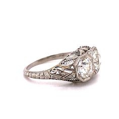 This Platinum ring features 2 diamonds totaling 2.0ct, VS2 clarity, and I color. Surrounding each of the diamonds are an octagon milgrain border and both stones are pave set. Along the body of the shank is filigree and flowers that are hand engraved with leaves and scroll work. This ring measures 9.70mm long on the head, and 14.61 wide as well. It measures 6.5mm off the top of the finger.Ring size:6.25US--Please reference our policy for more details-- Luxury Three Stone Octagon Ring, Luxury Octagon Three Stone Ring, Three-stone Octagon Diamond Ring, Diamond Three-stone Ring With Octagon Shape, Luxury Octagon Diamond Ring With Single Cut Diamonds, Three Stone Diamond Ring, Octagon Shaped, White Gold Octagon Three Stone Ring, White Gold Three Stone Octagon Rings, Classic Octagon Ring With Diamond Accents