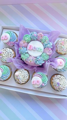 cupcakes decorated with pastel icing on a white tray next to pink and blue striped wallpaper