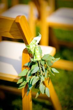 an outdoor ceremony with wooden chairs and greenery tied to the back of each chair