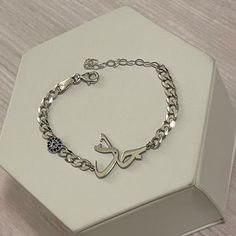 a silver bracelet with an arabic letter and blue crystal beads on it sitting in a white box