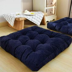 two blue cushions sitting on top of a wooden floor next to a table and chair