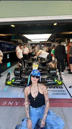 a woman sitting on the ground in front of a race car