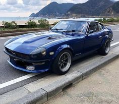 a blue sports car is parked on the side of the road next to the ocean