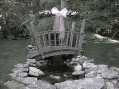 a wooden bridge over a small creek with flowers on it and a bow tied to the top