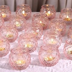 there are many pink glass bowls on the table with lit candles in them and one is filled with gold flakes