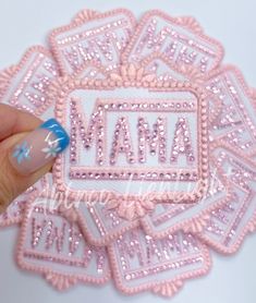 a hand holding a pink and white sticker with the word mama on it