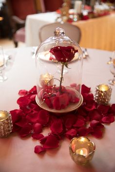 a rose in a glass dome on top of a table with candles and flowers around it