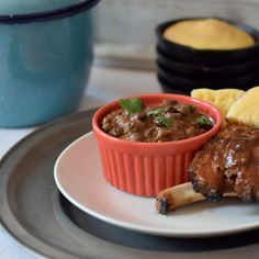 a plate topped with meat and potatoes next to a bowl of sauce on the side