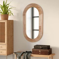 a mirror hanging on the wall next to a wooden table with luggage and a potted plant