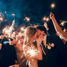 a bride and groom kiss as they are surrounded by their guests with sparklers in the air