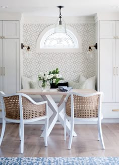 two chairs and a table with flowers on it in front of a wall that has a arched window