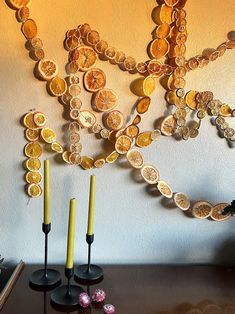 two candles are sitting on a table with some coins hanging from the wall behind them