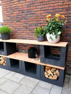 a wooden shelf sitting next to a brick wall filled with potted plants and logs