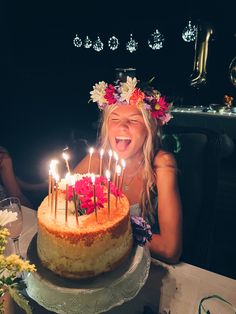 a woman sitting in front of a cake with lit candles on it and flowers around her head