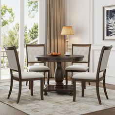 a dining table with four chairs and a bowl of fruit on it in front of a window