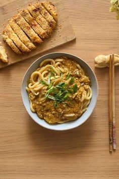 a bowl filled with noodles next to some bread and chopsticks on a table