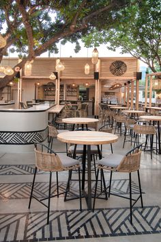 an outdoor dining area with tables and chairs under a tree in front of a bar