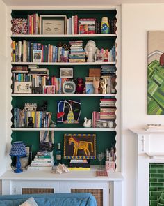 a living room filled with lots of books on top of a green book shelf next to a fireplace