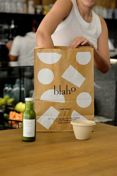 a woman holding a brown paper bag on top of a table next to a cup