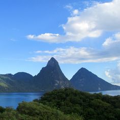 the mountains are covered in green vegetation and blue sky with white clouds above them, as well as water below