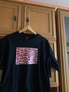 a black t - shirt with red and white designs on it hanging from a wooden closet