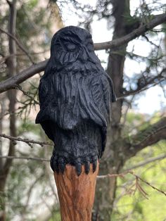 a statue of an owl sitting on top of a wooden post in the woods,