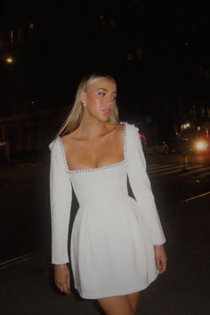 a woman in a white dress walking down the street at night with her hand on her hip