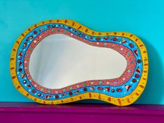 a decorative mirror sitting on top of a purple shelf next to a blue and yellow wall