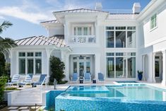 a large white house with a pool in the front yard and lounge chairs around it