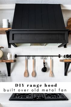 a stove top oven sitting under a black hood over an oven with utensils hanging from it