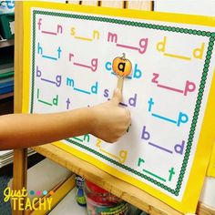 a child's hand holding a wooden stick in front of a white board with letters on it