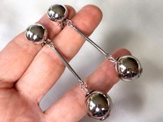 "Vintage 70s elegant and sleek platinum silver tone cocktail earrings featuring  polished silver tone balls suspended from fine long silver tone bars and round silver tone button clips. The  silver bubbles are are 2 cm (0.8\") in diameter,the diameter of silver hollow button clips 1.2 cm (0.5\") the total length is 9 cm (3.5\") , weight 20 grams and they are very comfortable to wear and in excellent vintage condition (NOS from Italy) For more vintage jewellery please visit my Etsy shop: http://vintageviomar.etsy.com SHIPPING  UK -Royal Mail First Class  (delivery aim 1- 2 days) Everywhere Else - Royal Mail International Tracked and Signed  (delivery aim 7-14 days) INTERNATIONAL BUYERS-PLEASE NOTE: Import duties,taxes and charges are not included in the item price or shipping cost.These cha Long Silver Earrings, Cocktail Earrings, Silver Button, Ball Earrings, Gold Statement Earrings, Bohemian Bracelets, Polish Silver, Silver Buttons, Silver Bars