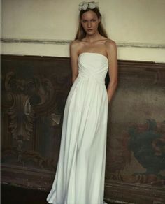 a woman standing in front of a wall wearing a white dress with a flower crown on her head