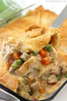 a spoonful of chicken pot pie with peas and carrots on it, in a casserole dish