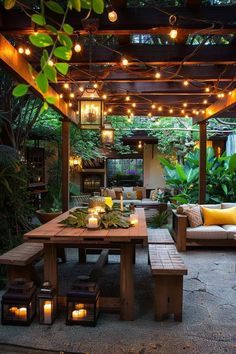 an outdoor dining area with lights strung from the ceiling and wooden benches, surrounded by greenery