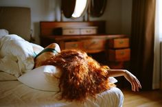 a woman laying on top of a bed covered in white sheets and pillows next to a dresser