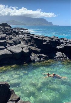 two people are swimming in the ocean near some rocks and water with an island in the background