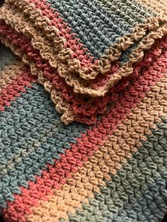 a multicolored crocheted blanket laying on top of a table next to a pillow