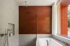 a bathroom with a bathtub, shower head and red tiled wall next to a window