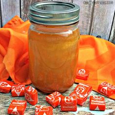 a jar filled with candy sitting on top of a wooden table next to orange cloth