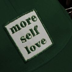 there is a patch that says more self love on the back of a green hat